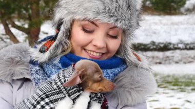 Köpeğiyle oynayan genç bir kadın, pinscher ratter prazsky krysarik, kış havasında dışarıda. Dişi köpek yavrusuna sevgiyle sarılıyor..
