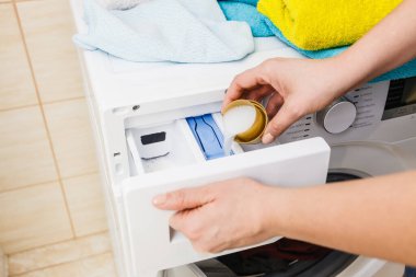 Çamaşır deterjanı ve ölçü kabının makineye dökülmesi. Ev işleri, çamaşır yıkama, obezite konsepti..