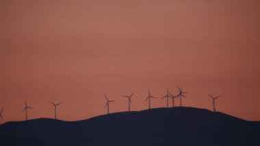 Akşam manzarası. Gün batımında tepede rüzgâr türbinleri çiftliği.