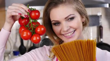 Komik kadın elinde uzun makarna ve taze domatesle spagetti pişirmeyi düşünüyor..