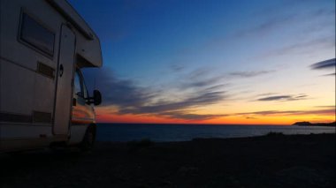 Gün batımında, karavanın üzerinde hareket eden bulutlar deniz kenarında kamp kuruyor, gece çöküyor. Karavanla seyahat ediyorum. Karavan tatili. Doğa ve faaliyetler.