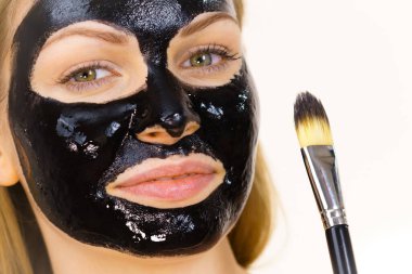 Siyah detoks detoks ile uygulanan genç bir kadın maskesini yüzüne doğru sıyırdı. Deriyle ilgilenen bir kız. Güzellik tedavisi. Cilt bakımı.