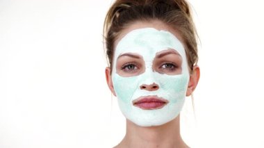 Yüzünde beyaz yeşil çamur maskesi olan genç bir kadın. Genç kız yağlı cildiyle ilgileniyor, gözenekleri temizliyor. Güzellik tedavisi. Cilt bakımı.