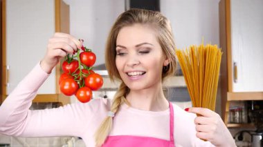 Komik kadın elinde uzun makarna ve taze domatesle spagetti pişirmeyi düşünüyor..