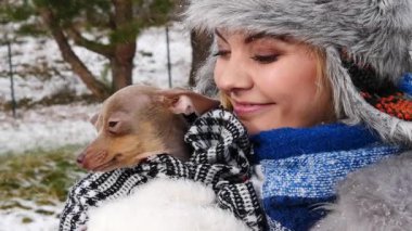 Köpeğiyle oynayan genç bir kadın, pinscher ratter prazsky krysarik, kış havasında dışarıda. Dişi köpek yavrusuna sevgiyle sarılıyor..
