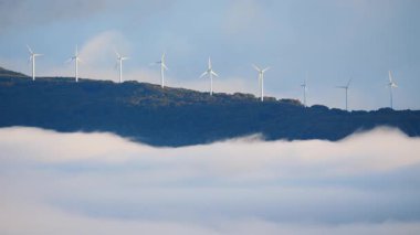 Sabahları bulutların üstündeki tepede rüzgâr türbinleri çiftliği. Koruma ve sürdürülebilir enerji kavramı.