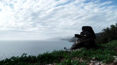 Akdeniz 'de, kayalık deniz kıyısında uzanan yürüyüş ayakkabılarıyla hareket eden bulutların hızlanması. Deniz kenarındaki patikada yürüyüş. Seyahat, macera konsepti.