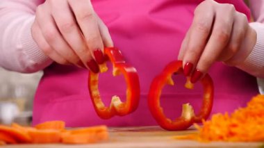 Salata yapan kişi. Kadın eli kesme tahtasında iki parça kırmızı dolma biber halkası gösteriyor..