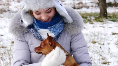 Genç bir kadın kış havasında yavru köpeğiyle dışarıda oynuyor..