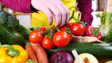 Diğer sebzelerin önünde bitkinin üzerinde kiraz domateslerini gösteren tanınmamış bir kadın eli. Sağlıklı yeme kavramı.