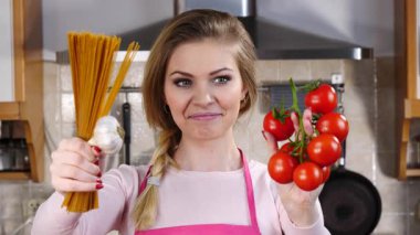 Komik kadın elinde uzun makarna ve taze domatesle spagetti pişirmeyi düşünüyor..
