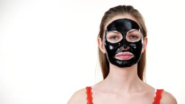 Karbonhidrat maskesi takmış genç bir kadın. Yüzünün, beyazının farklı bölgelerine parmağıyla işaret ediyor. Genç kız siyah gözenekleri temizliyor. Güzellik tedavisi. Cilt bakımı.