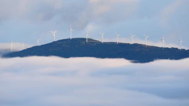 Sabahları bulutların üstündeki tepede rüzgâr türbinleri çiftliği. Koruma ve sürdürülebilir enerji kavramı.