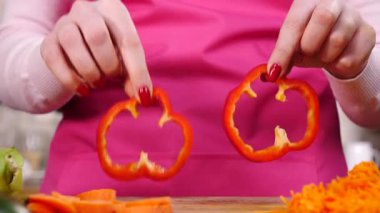 Salata yapan kişi. Kadın eli kesme tahtasında iki parça kırmızı dolma biber halkası gösteriyor..