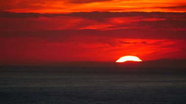 Deniz üzerinde gün batımında kızıl gökyüzü. Güneş ufukta batıyor. Akşam doğa manzarası.