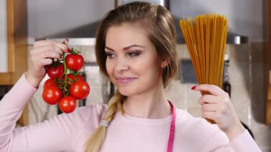 Komik kadın elinde uzun makarna ve taze domatesle spagetti pişirmeyi düşünüyor..