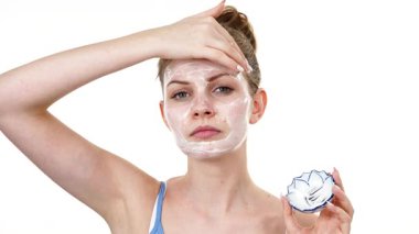 Maske takan genç bir kadın yüzüne nemlendirici krem sürüyor. Cilt nemlendiricisine dikkat eden bir kız. Cilt bakımı.