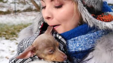 Köpeğiyle oynayan genç bir kadın, pinscher ratter prazsky krysarik, kış havasında dışarıda. Dişi köpek yavrusuna sevgiyle sarılıyor..