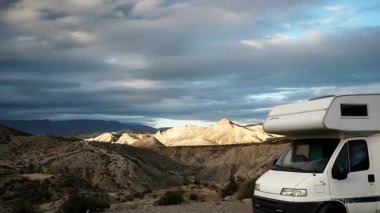 Dağların üzerinde hareket eden tüylü bulutlar ve Tabernas Çölü, Almerya Bölgesi, Endülüs İspanya 'da kamp yapan karavan aracı..