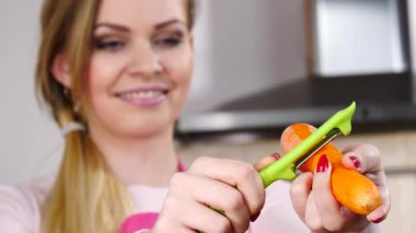 Mutluluktan havucu soyan neşeli kadın mutfak soyucusu kullanarak sebze pişirmeye hazırlanıyor..