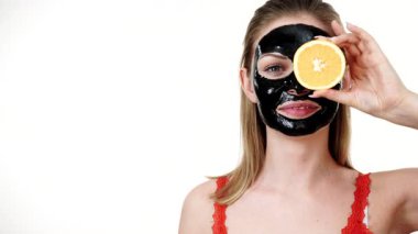 Yüzünde karbonhidrat maskesi olan genç bir kadın portakal meyvesi tutuyor, gözü kapalı, beyaz üzerinde. Güzellik tedavisi. Cilt bakımı.