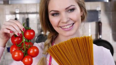 Komik kadın elinde uzun makarna ve taze domatesle spagetti pişirmeyi düşünüyor..