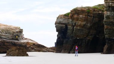 Kameralı bir kadın, Kuzey İspanya 'nın Lugo, Galiçya eyaletindeki katedrallerin plajlarını, playa las kategorilerini ziyaret ediyor. Turistler uçurum oluşumlarından seyahat fotoğrafları çekerler..