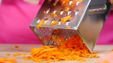 Kadının el rendeleyici havucu mutfak tahtasında yavaş çekimde sebze rendesi kullanarak yakın çekim..