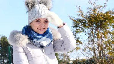 Karlı kış mevsiminde açık havada şapkalı, kalın giysiler giyen genç bir kadın uzaktan bakıyor.