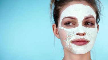 Yüzünde beyaz kurumuş çamur maskesi olan genç bir kadın maviliğe karşı çıkartılıyor. Yağlı ciltle ilgilenen genç bir kız. Güzellik tedavisi. Cilt bakımı.