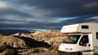 Dağların üzerinde hareket eden tüylü kara bulutlar ve Tabernas Çölü, Almerya Bölgesi, Endülüs İspanya 'da kamp yapan karavan aracı..