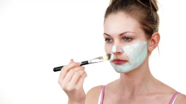 Yüzüne yeşil çamur maskesi dayayan genç bir kadın. Genç kız yağlı cildiyle ilgileniyor, gözenekleri temizliyor. Güzellik tedavisi. Cilt bakımı.