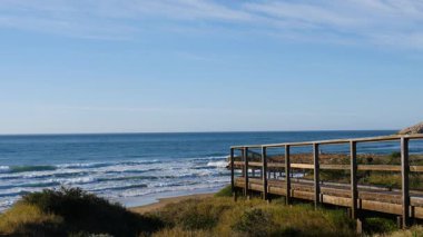 Sahil manzarası, denize giden ahşap yolu olan deniz kıyısı, dalgalar ağır çekimde hareket ediyor. Cala Magre Sahili, Calique Bölgesel Parkı, Murcia Bölgesi İspanya.