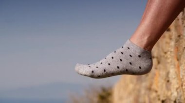 Tatil ve tasasız. Mavi gökyüzüne karşı noktalı çoraplı kadın ayakları. Taş duvarda oturan kadın, bacaklarını sallıyor, güneşli yaz gününde güneşin tadını çıkarıyor..