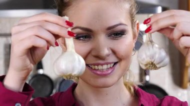 Mutlu bir kadın, sarımsak küpesiymiş gibi davranarak eğleniyor. Sağlıklı sebze, diyet yiyecek konsepti.