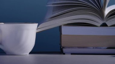 Tatillerde kitap okumak. Kahve fincanı ve kitaplar açık masada. Kitap sayfaları rüzgarda çırpınıyor.