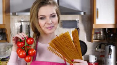 Komik kadın elinde uzun makarna ve taze domatesle spagetti pişirmeyi düşünüyor..