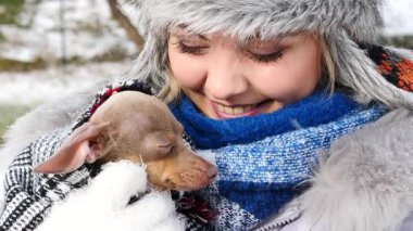 Köpeğiyle oynayan genç bir kadın, pinscher ratter prazsky krysarik, kış havasında dışarıda. Dişi köpek yavrusuna sevgiyle sarılıyor..