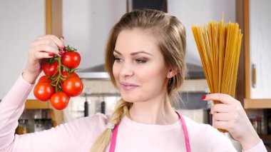 Komik kadın elinde uzun makarna ve taze domatesle spagetti pişirmeyi düşünüyor..