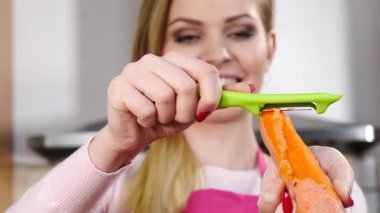 Mutluluktan havucu soyan neşeli kadın mutfak soyucusu kullanarak sebze pişirmeye hazırlanıyor..