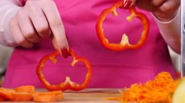 Salata yapan kişi. Kadın eli kesme tahtasında iki parça kırmızı dolma biber halkası gösteriyor..