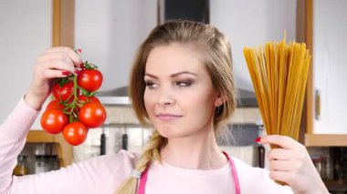 Komik kadın elinde uzun makarna ve taze domatesle spagetti pişirmeyi düşünüyor..