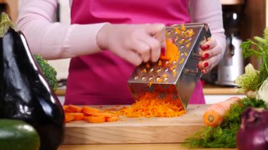 Kadının el rendeleyici havucu mutfak tahtasında yavaş çekimde sebze rendesi kullanarak yakın çekim..