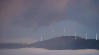 Sabahları bulutların üstündeki tepede rüzgâr türbinleri çiftliği. Koruma ve sürdürülebilir enerji kavramı.