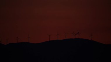 Akşam manzarası. Gün batımında tepede rüzgâr türbinleri çiftliği.