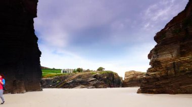 Kameralı bir kadın, Kuzey İspanya 'nın Lugo, Galiçya eyaletindeki katedrallerin plajlarını, playa las kategorilerini ziyaret ediyor. Turistler uçurum oluşumlarından seyahat fotoğrafları çekerler..