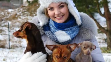 Üç köpeğiyle oynayan genç bir kadın, pinscher ratter prazsky krysarik, dachshund, kış havasında dışarıda..