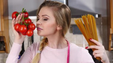 Komik kadın elinde uzun makarna ve taze domatesle spagetti pişirmeyi düşünüyor..