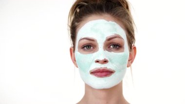 Yüzünde beyaz yeşil çamur maskesi olan genç bir kadın. Genç kız yağlı cildiyle ilgileniyor, gözenekleri temizliyor. Güzellik tedavisi. Cilt bakımı.