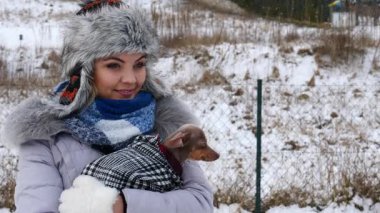 Köpeğiyle oynayan genç bir kadın, pinscher ratter prazsky krysarik, kış havasında dışarıda. Dişi köpek yavrusuna sevgiyle sarılıyor..